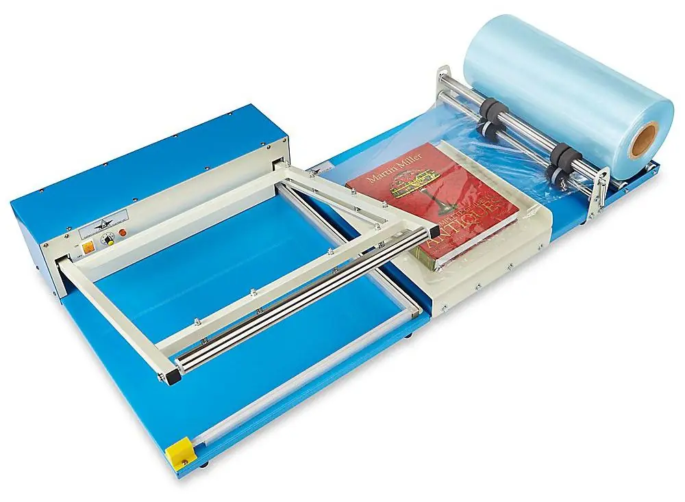 A blue tabletop L-bar sealer with a hinged L-shaped seal frame, a book in folded film, and a film roll on the right.